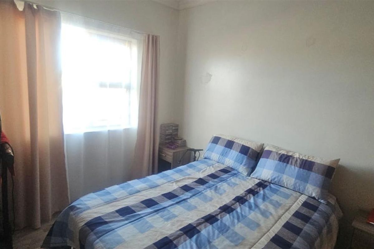 A standard bedroom featuring a window with curtain rails and plain wall finishes, requiring minor cosmetic updates.