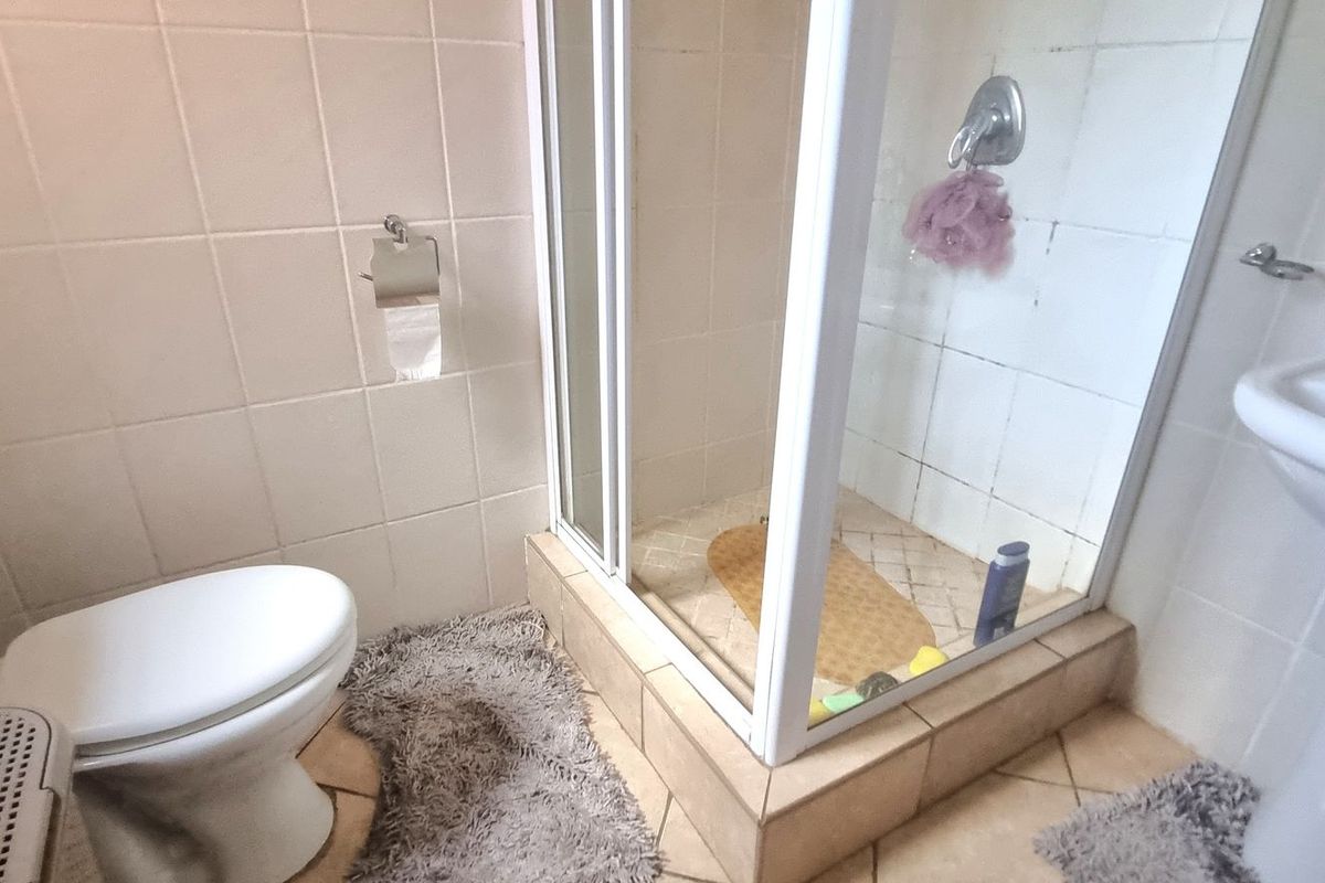 A functional bathroom featuring a corner shower enclosure, pedestal basin, and toilet with neutral wall tiling.