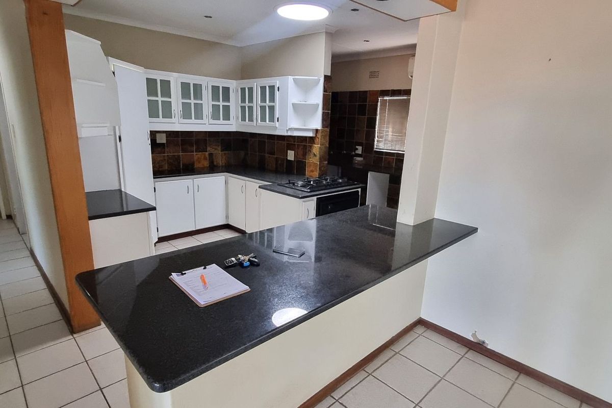 A functional kitchen featuring granite countertops, built-in white cabinetry, a gas hob, and a breakfast bar, with tiled flooring throughout.