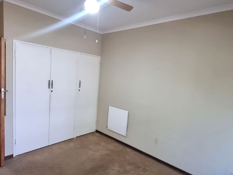 A spacious bedroom featuring built-in cupboards, a ceiling fan, and wall-mounted heating, offering a neutral canvas ready for personalization.