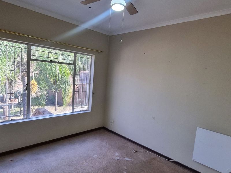 An empty bedroom featuring a ceiling fan, wall-mounted heater, and security bars on the window, offering a blank canvas for personalization.