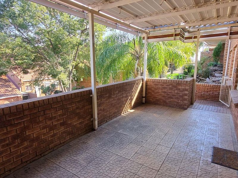 A spacious covered balcony featuring brick walls, tiled flooring, and a metal roof structure, offering an open outdoor area with neighborhood views.
