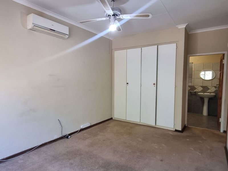 An empty bedroom featuring built-in cupboards, a ceiling fan, and an air conditioning unit, with an adjoining bathroom visible.