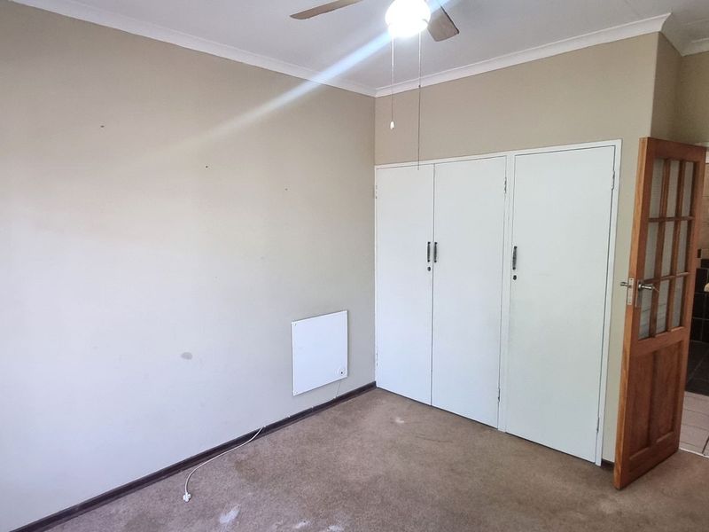An empty bedroom featuring built-in cupboards, a ceiling fan, and a wall-mounted heater, with direct access to an en-suite bathroom.