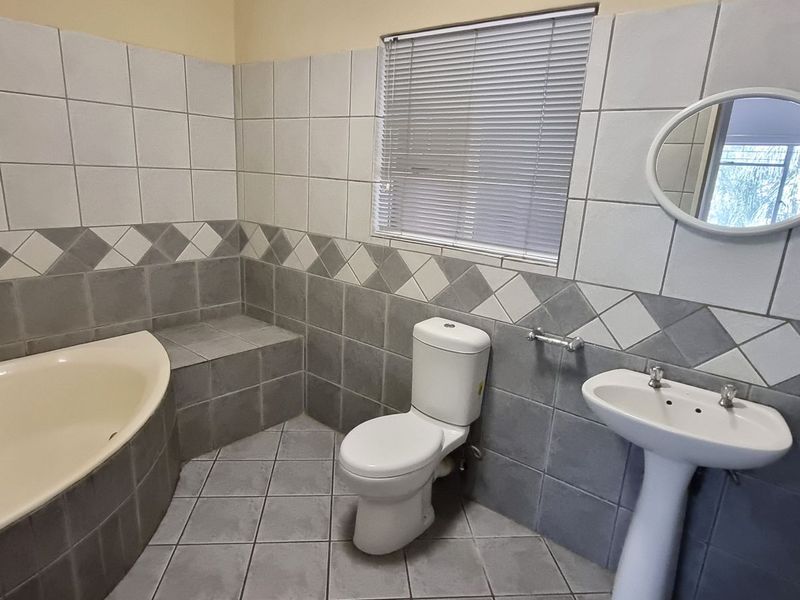 A functional bathroom featuring a built-in corner bathtub, pedestal basin, toilet, and tiled finishes throughout.
