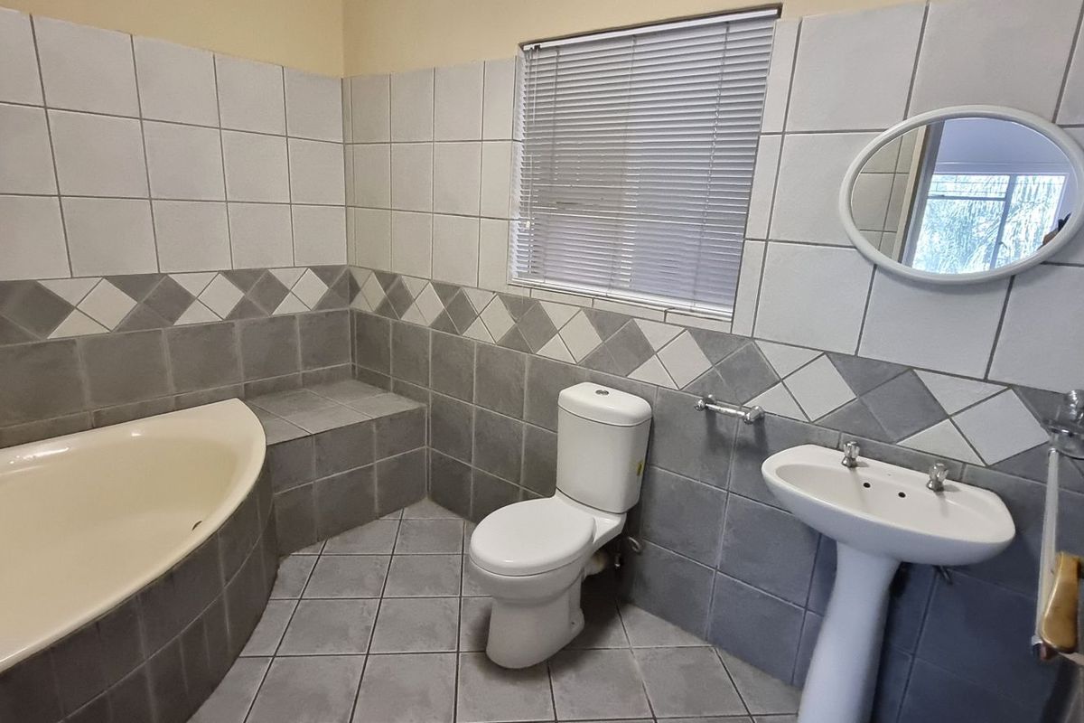 A functional bathroom featuring a built-in corner bathtub, pedestal basin, toilet, and tiled finishes throughout.