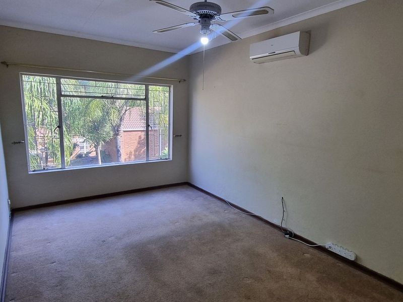 An empty bedroom featuring a ceiling fan, wall-mounted air conditioning unit, and large window, providing a blank canvas for potential renovation or staging.