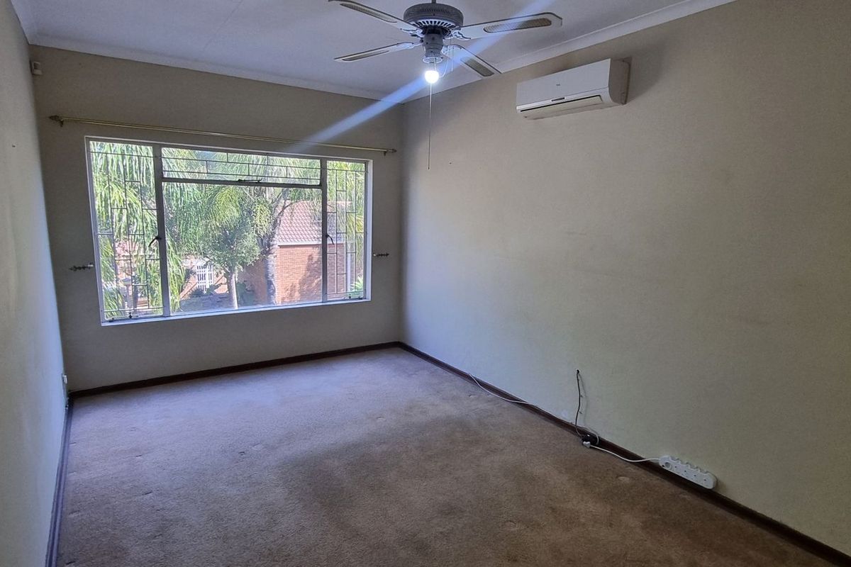 An empty bedroom featuring a ceiling fan, wall-mounted air conditioning unit, and large window, providing a blank canvas for potential renovation or staging.