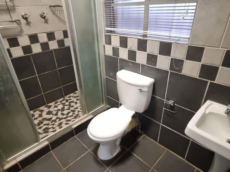 A compact bathroom featuring a shower enclosure, pedestal basin, and toilet, finished with dark and light checkered wall tiling.
