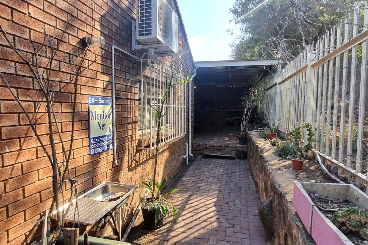 Rear exterior area featuring a paved walkway, brick wall, security fencing, and a covered patio space with an outdoor sink.