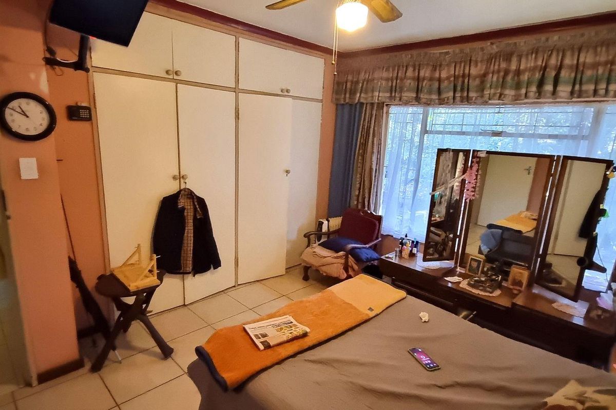 A bedroom featuring built-in floor-to-ceiling cupboards, tiled flooring, and a large window with curtain pelmet.
