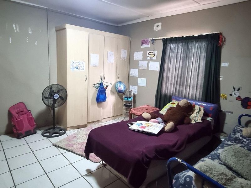 A bedroom featuring tiled flooring and a built-in wardrobe, currently showing signs of wear on the wall surfaces.