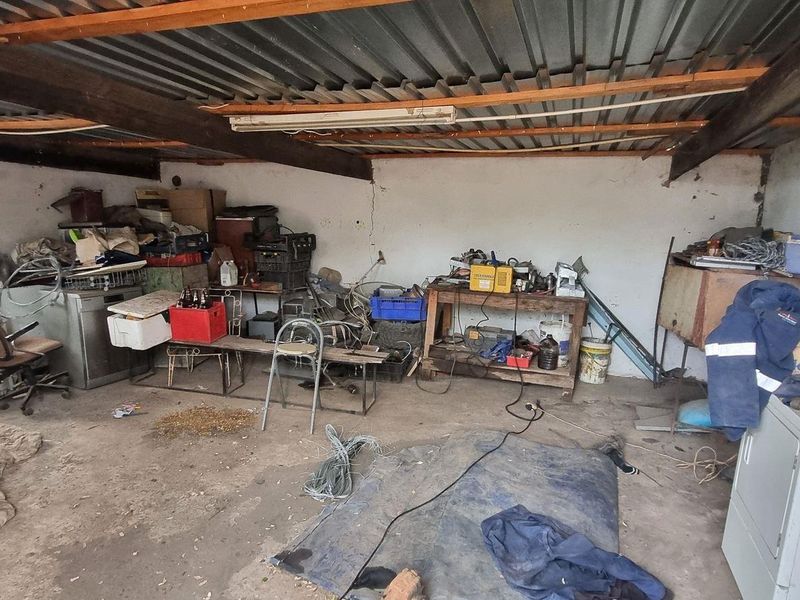 A spacious garage area featuring exposed timber beams, corrugated metal roofing, and concrete flooring, offering significant potential for workshop or storage use.