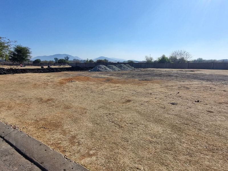 A wide-angle view of a vacant residential plot featuring a perimeter wall and dry grass, ready for development.
