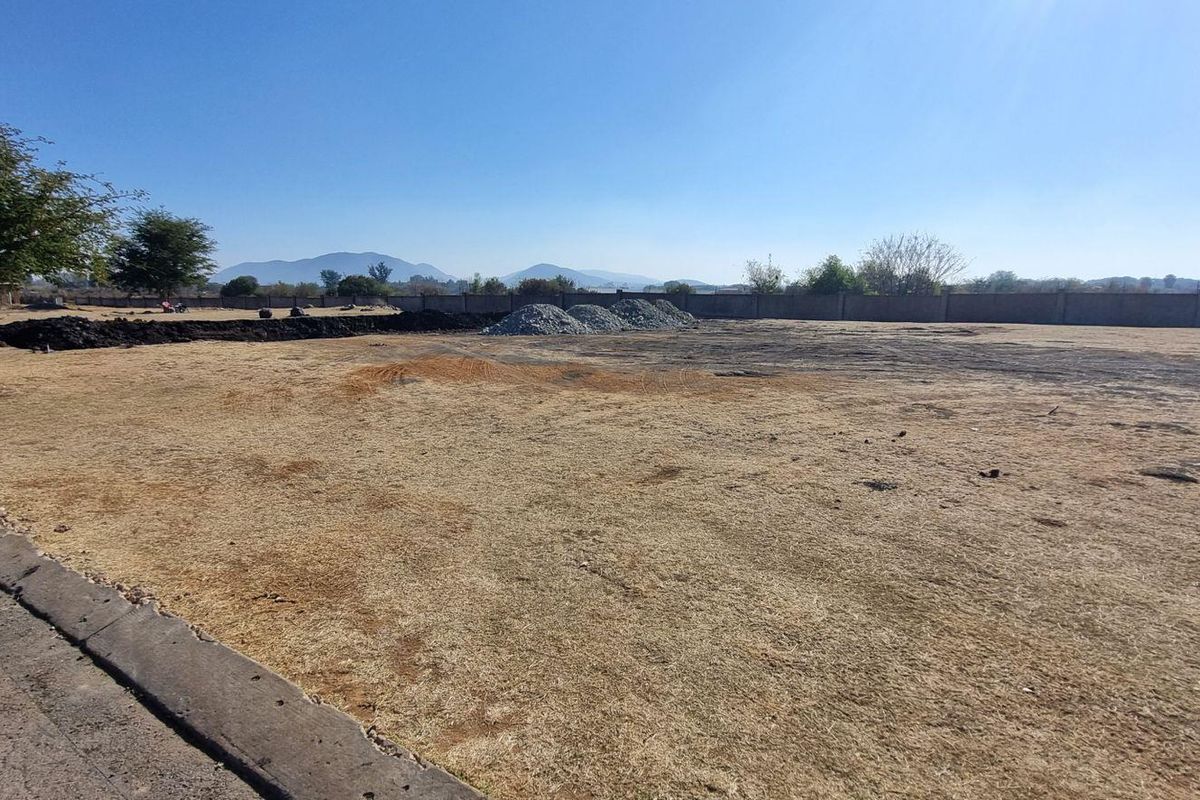 A wide-angle view of a vacant residential plot featuring a perimeter wall and dry grass, ready for development.