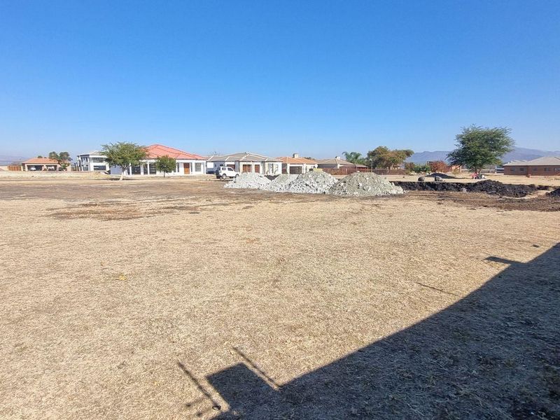 A vacant residential plot featuring dry grass, a perimeter wall with electric fencing, and surrounding neighborhood views.