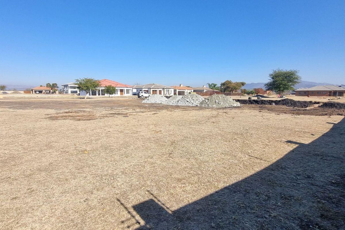 A vacant residential plot featuring dry grass, a perimeter wall with electric fencing, and surrounding neighborhood views.