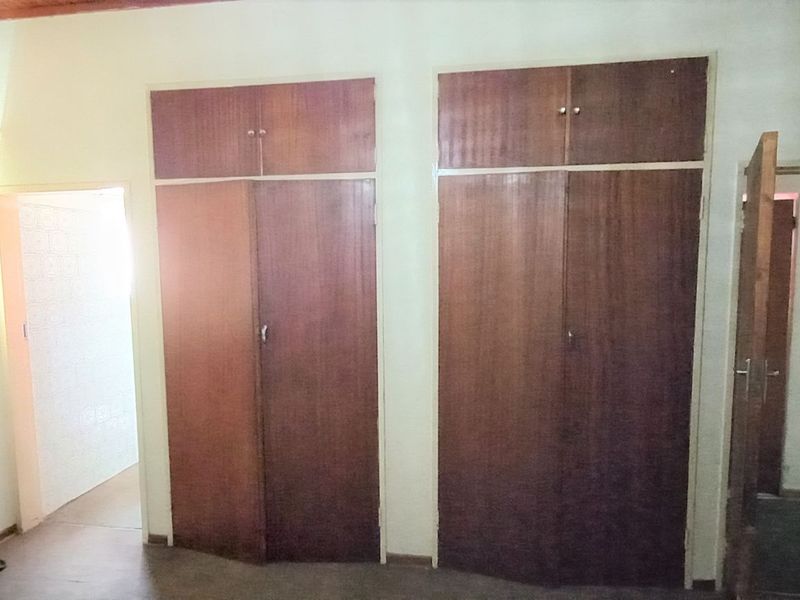 A bedroom featuring built-in wooden cupboards and neutral wall finishes, offering a blank canvas for potential renovation or interior design updates.