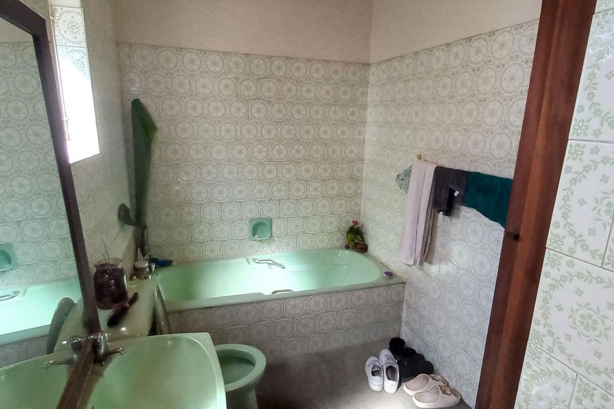 A dated bathroom featuring a built-in bathtub, pedestal basin, and toilet with vintage patterned wall tiles.