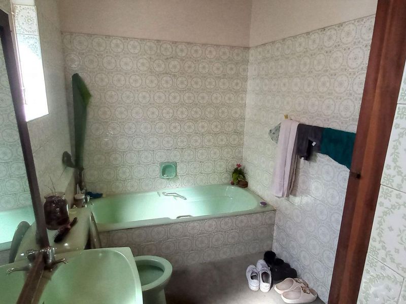 A dated bathroom featuring a built-in bathtub, pedestal basin, and toilet with vintage patterned wall tiles.