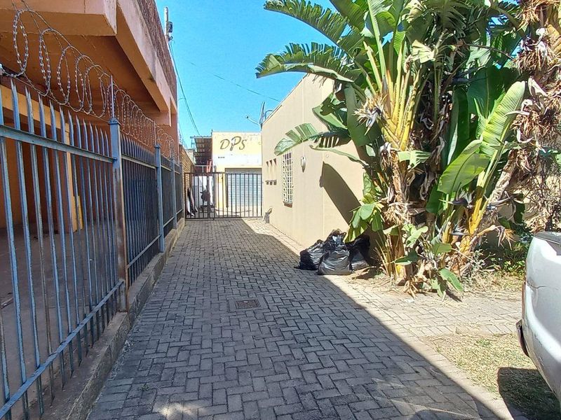 A narrow paved side passage featuring steel security fencing with razor wire and a gated entrance, showing signs of wear and maintenance needs.