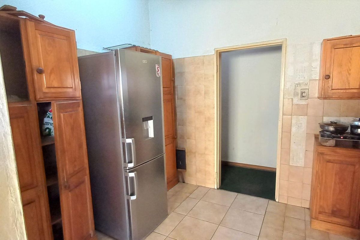 A dated kitchen featuring wooden cabinetry, tiled splashbacks, and tiled flooring, offering potential for a modern renovation.