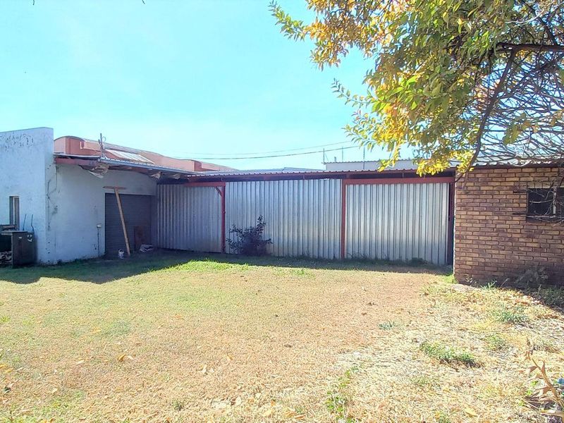 Rear view of the property featuring a large lawn area, brick wall sections, and corrugated metal cladding on the building exterior.