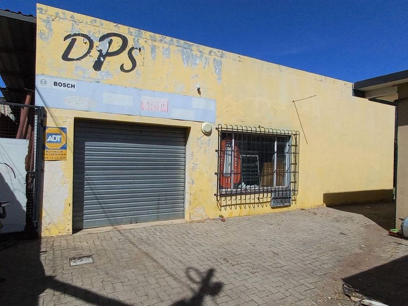 Commercial-style exterior facade featuring a roller shutter door, security bars, and paved frontage, showing significant signs of wear and peeling paint.