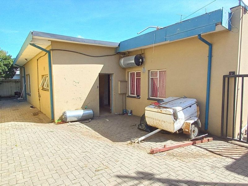 Rear exterior view of the property featuring paved driveway, security bars on windows, and external geyser unit with visible wear to the wall finish.