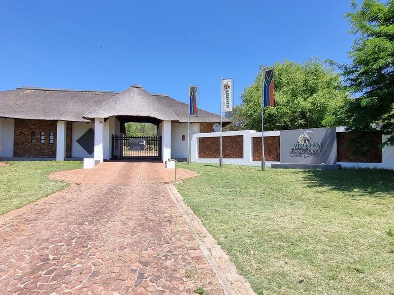 Front entrance view of the farm lodge featuring a thatched roof structure, stone masonry boundary walls, and a paved driveway leading to the main gate.