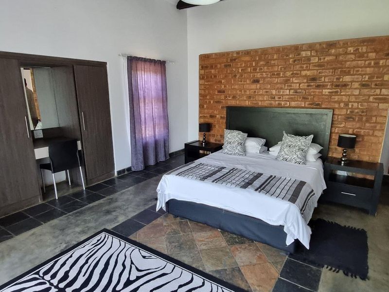 Spacious bedroom featuring an exposed brick accent wall, built-in wardrobe, and durable tiled flooring, offering a rustic yet comfortable living space.