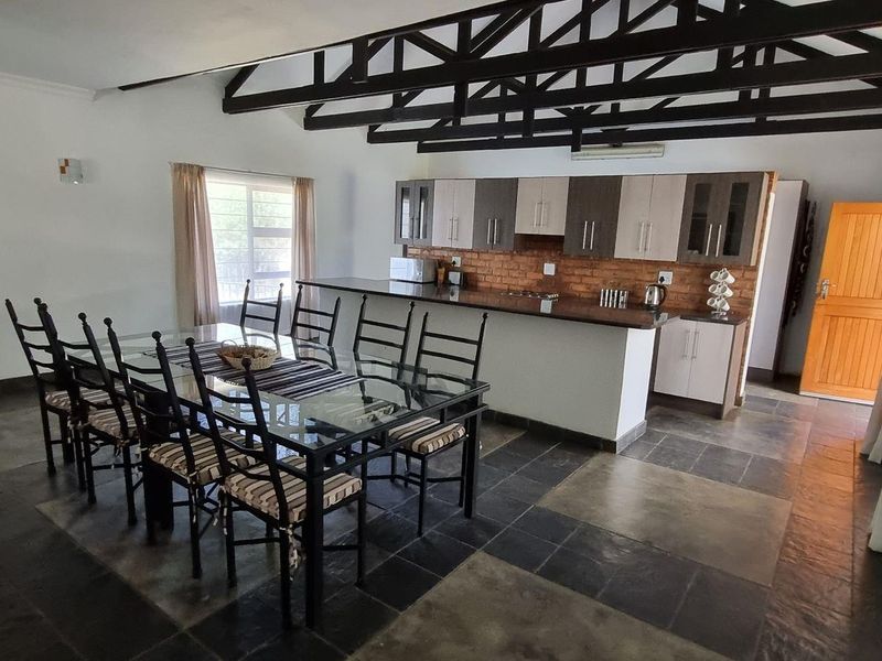 Spacious open-plan living and dining area featuring exposed timber roof trusses, slate flooring, and a kitchen with granite countertops and brick feature wall.