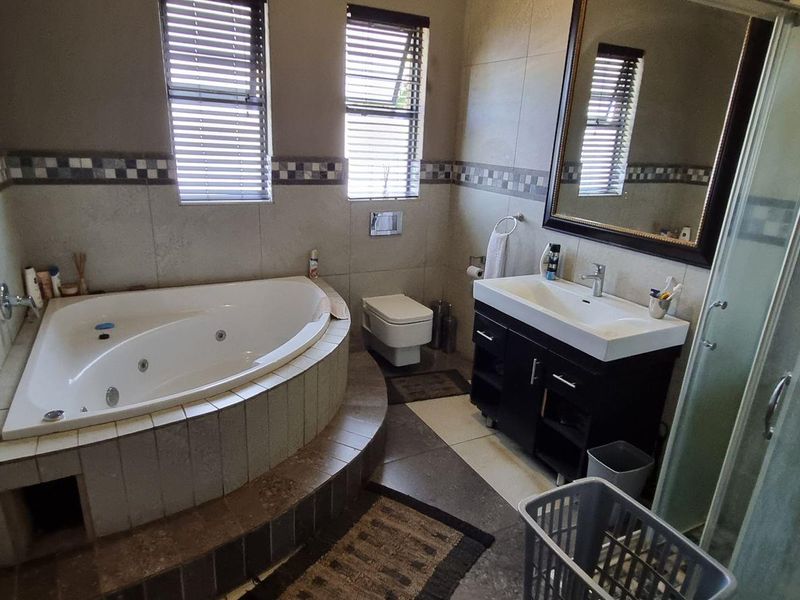 A functional bathroom featuring a corner spa bath, wall-mounted toilet, vanity with basin, and a separate glass shower enclosure with tiled finishes.