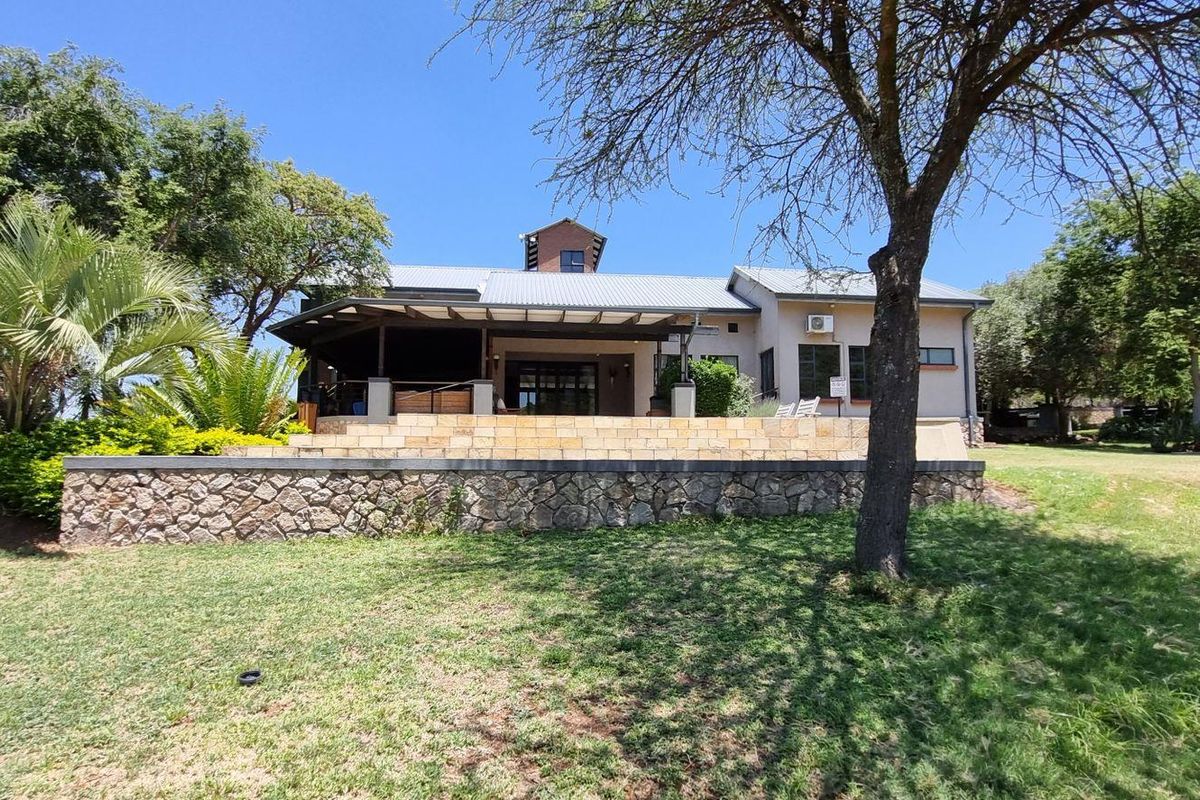 Rear view of the farm property featuring a stone retaining wall, a spacious covered patio, and a well-maintained garden area.