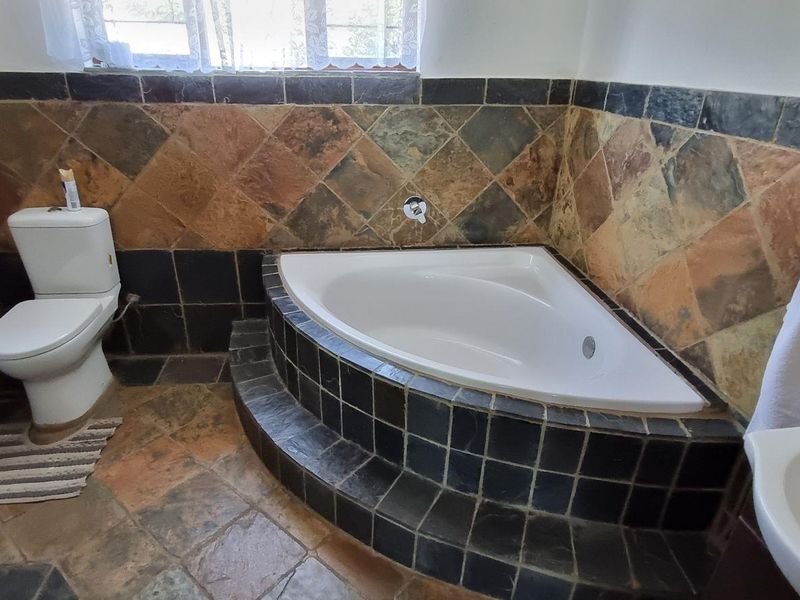 A functional bathroom featuring a corner bathtub, pedestal basin, and toilet, finished with rustic slate-style wall and floor tiling.