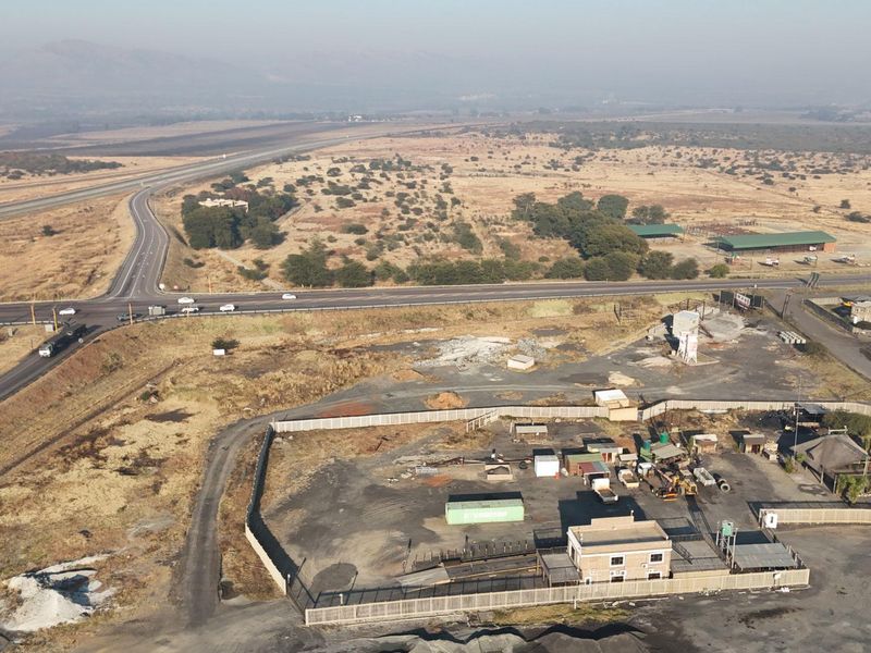 Aerial view of a commercial property site featuring a fenced yard, main building, and direct access to the adjacent highway infrastructure.