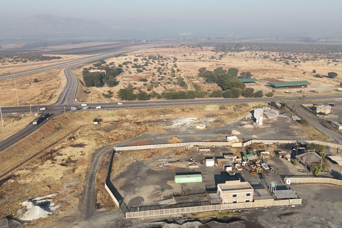 Aerial view of a commercial property site featuring a fenced yard, main building, and direct access to the adjacent highway infrastructure.