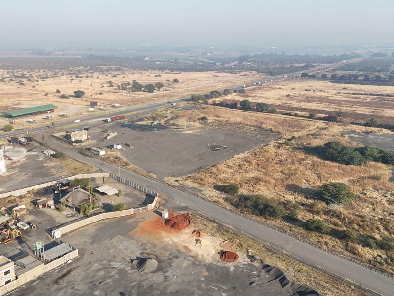 Aerial view of a commercial property featuring paved access, fenced perimeter, and strategic highway frontage in an open landscape setting.