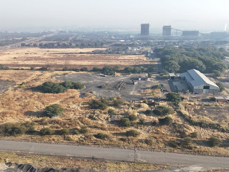 Aerial view of a commercial property featuring a large warehouse structure, paved yard space, and surrounding industrial land with road access.