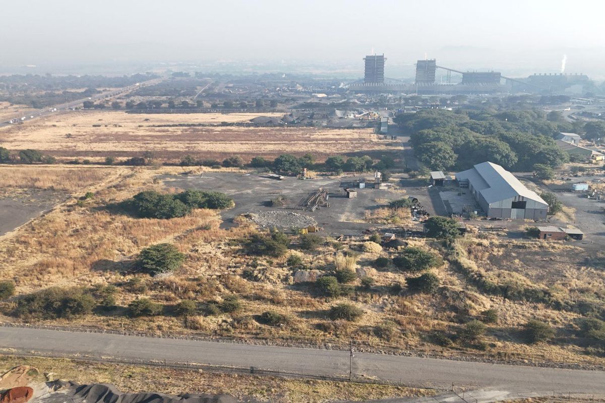 Aerial view of a commercial property featuring a large warehouse structure, paved yard space, and surrounding industrial land with road access.