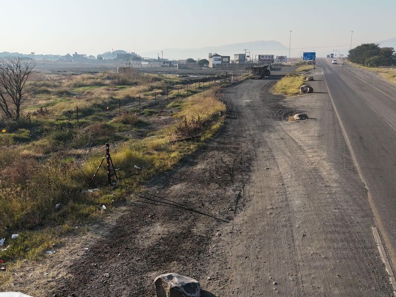 A view of the commercial property frontage showing the adjacent asphalt road, unpaved verge, and surrounding landscape.