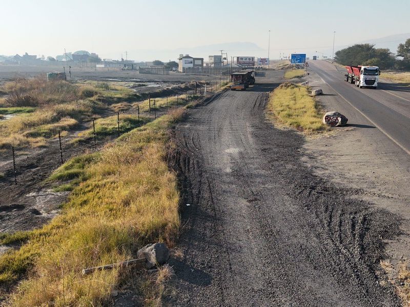 A view of a commercial property access point featuring an asphalt road, gravel shoulder, and perimeter electric fencing.