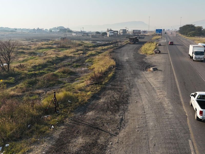 An elevated view of a commercial property frontage showing the adjacent asphalt road, unpaved verge, and surrounding landscape.