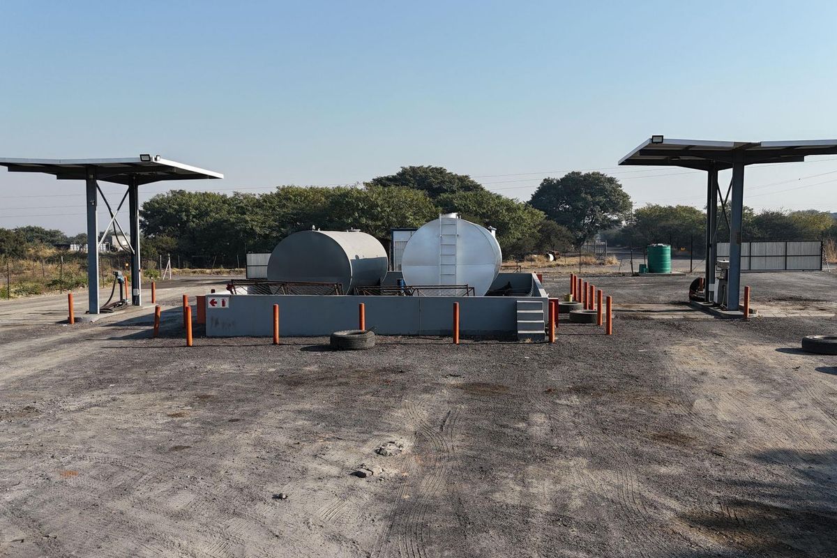 Commercial fuel depot area featuring two large storage tanks within a containment bund, protected by safety bollards and covered by dual pump canopies.