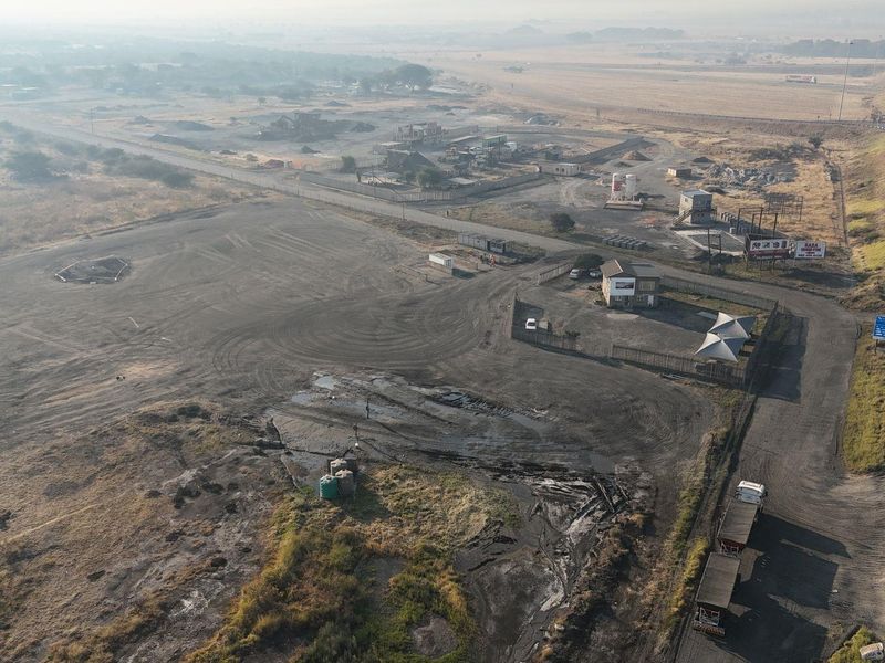 Aerial view of a large commercial land parcel with highway access, featuring a small office building and extensive undeveloped ground space.