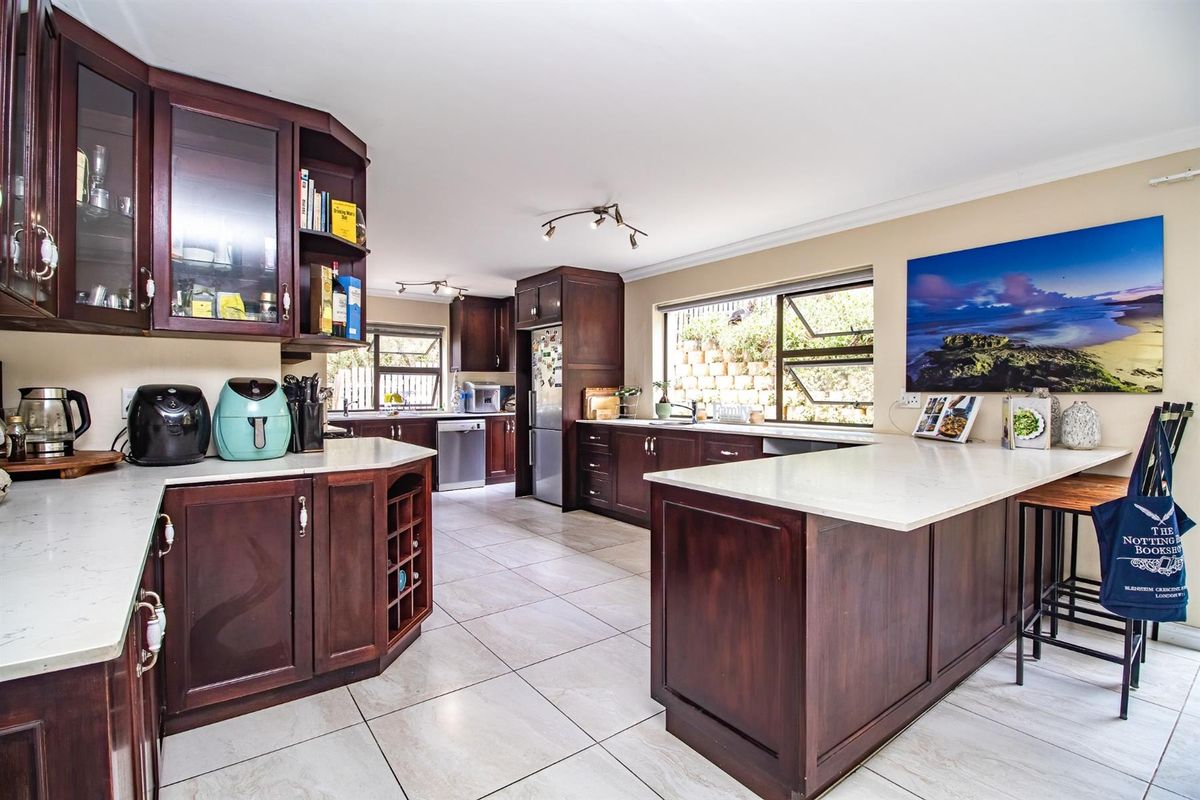 Spacious kitchen featuring dark wood cabinetry, light stone countertops, tiled flooring, and a breakfast bar island with integrated storage.
