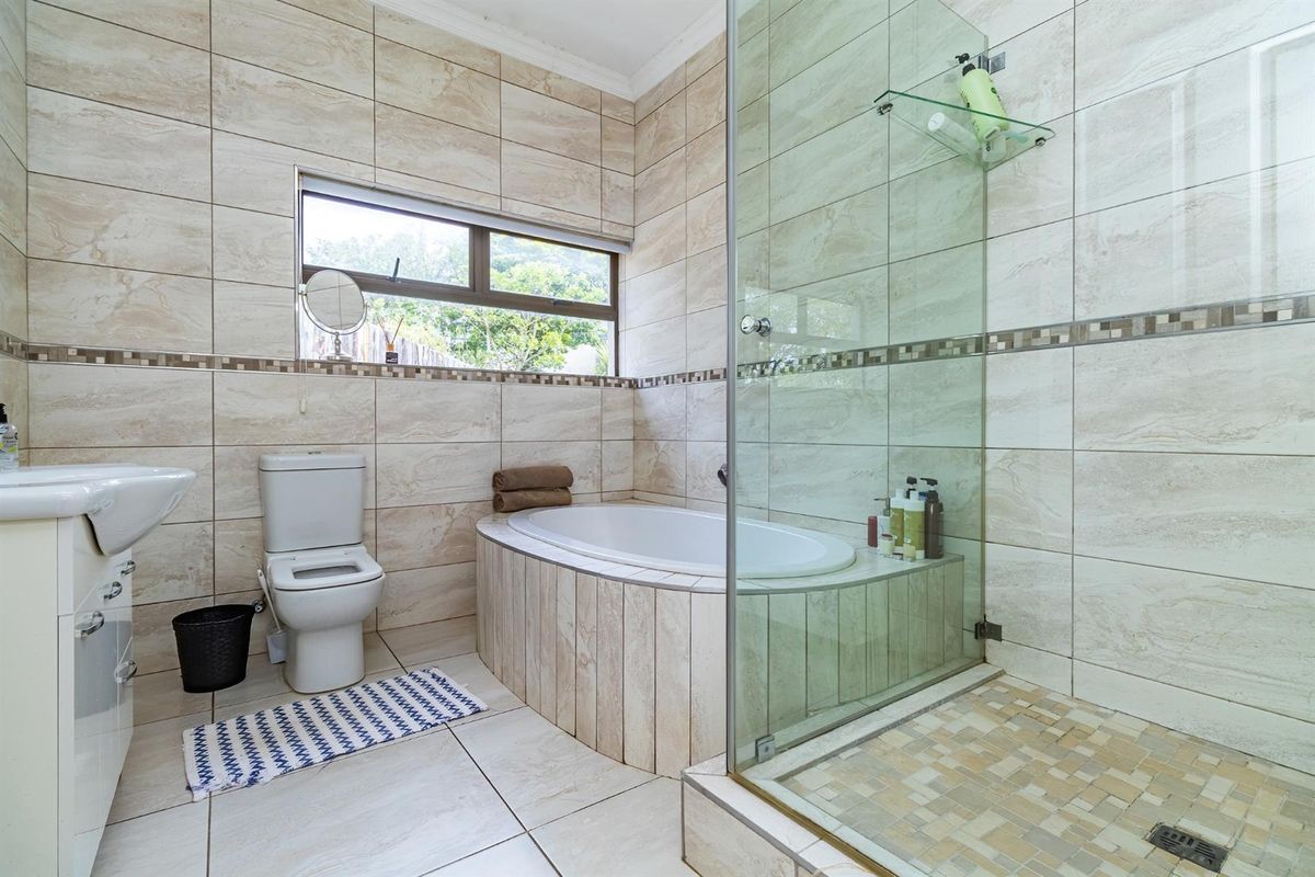 A well-maintained bathroom featuring a built-in bathtub, a separate glass-enclosed shower, a pedestal basin, and neutral floor-to-ceiling wall tiles.