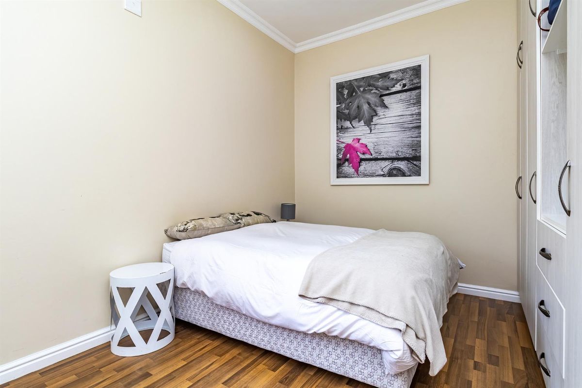 A compact bedroom featuring laminate wood flooring, crown molding, and a built-in wardrobe with modern hardware.