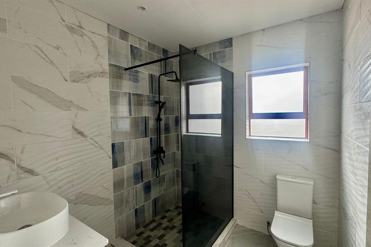 Modern bathroom featuring a walk-in shower with a black frame, contemporary vessel sink, and stylish marble-look wall tiling.