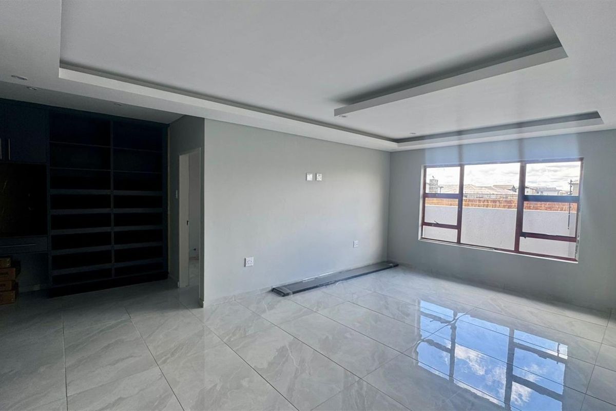 A bright, modern living room featuring polished marble-look floor tiles, recessed ceiling lighting, and built-in dark cabinetry.